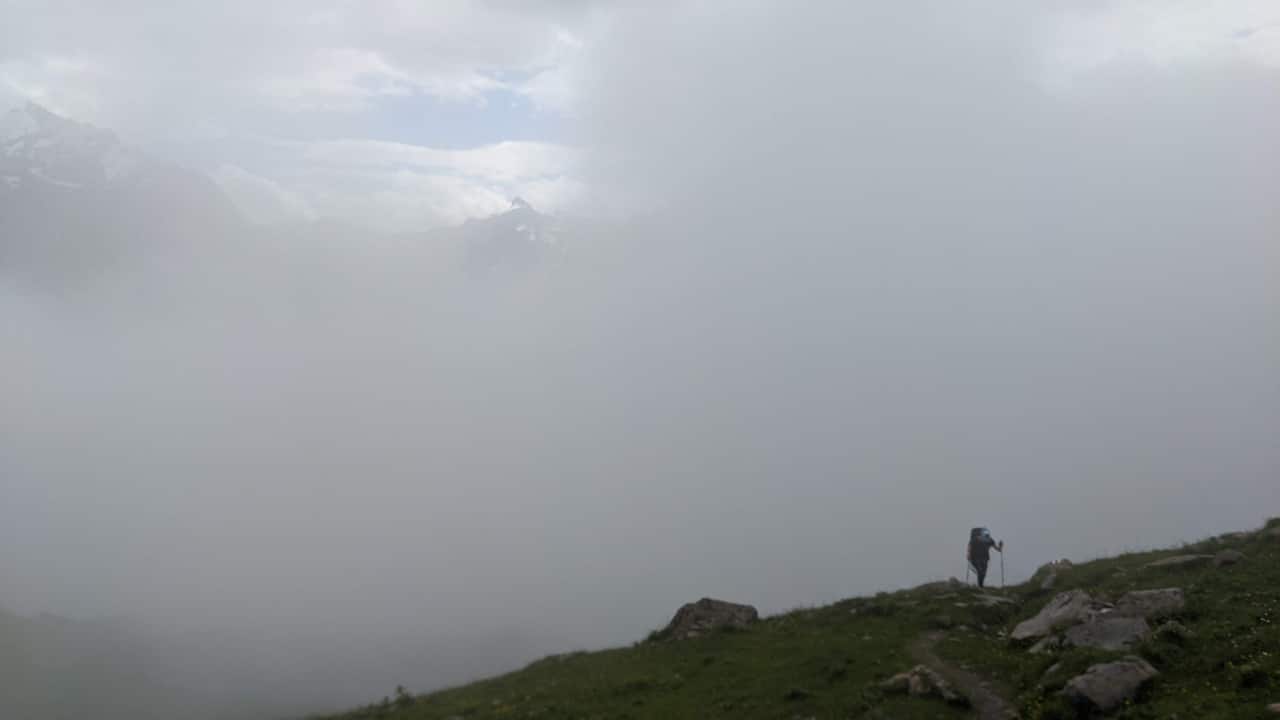 Solène hiking on Via Alpina from Kandersteg to Bunderchrine mountain pass. In the backgrund a fog wall.