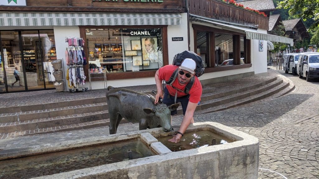 Matthias at a fountain with a statue of calf in the Swiss village Gstaad. In the background the windows of shops, among them a poster of luxury brand Channel.