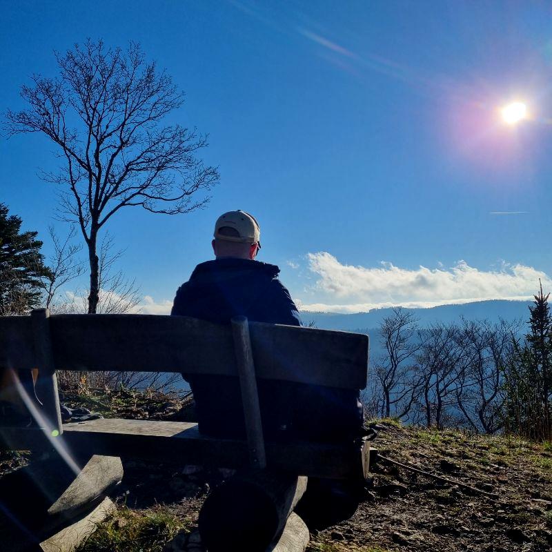 Mann sitzt auf der Bank auf dem Hirnichopf beim Nunningerberg und geniesst die Mittagssonne und die Aussicht