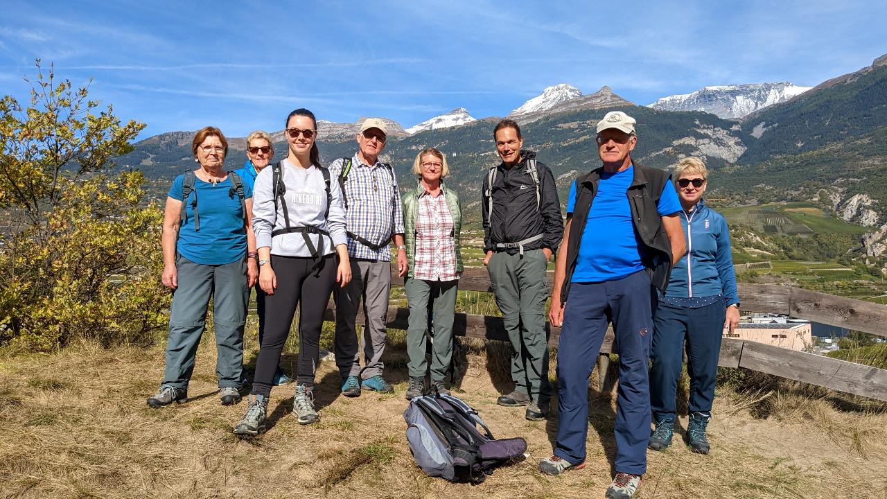 Acht Personen posieren auf dem Rebberg für ein Foto. Im Hintergrund sind Walliser Berge zu sehen.