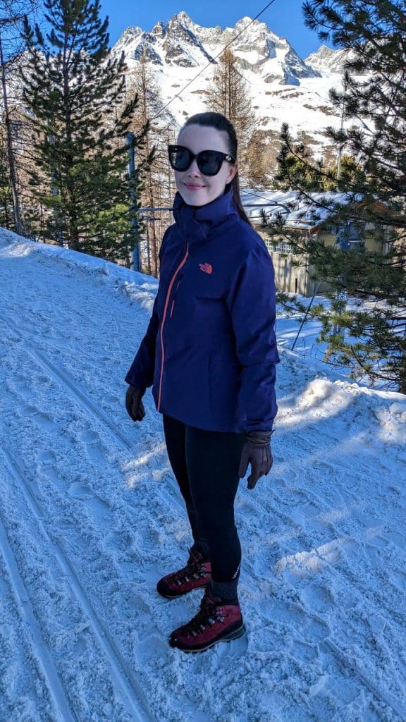 Solène lächelt in die Kamera. Es ist eine Nahaufnahme von Solène. Sie wandert auf dem schneebedeckten, aber gewalzten Winterwanderweg auf der Riffelalp.
