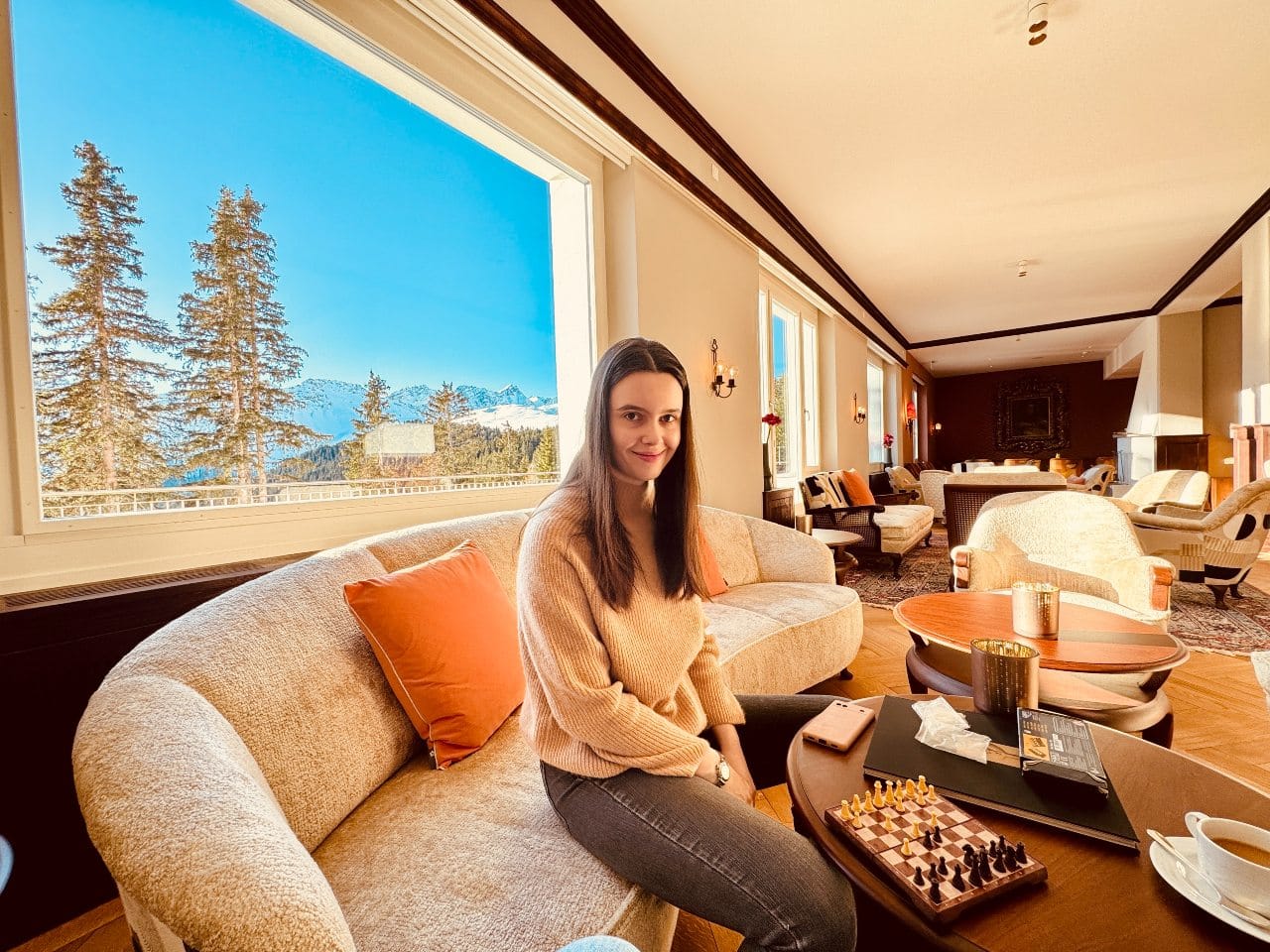 Solène sitzt vor der beeindruckenden Fensterfront im Salon des Hotel Prätschli und spielt Schach