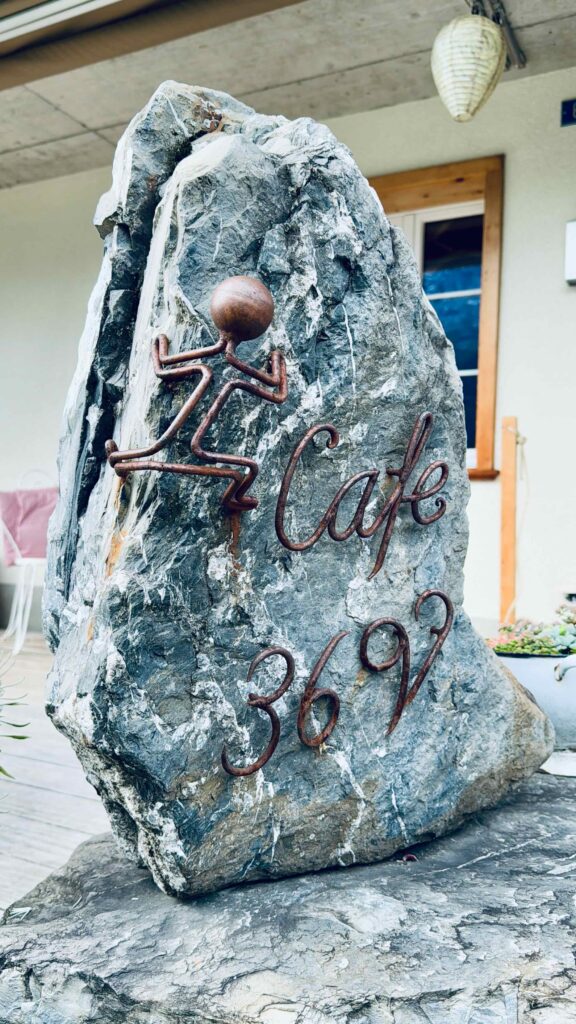 Ein markantes Felsenschild mit Eisen-Schriftzug "Café 3692" vor dem Eingang des Restaurants in Grindelwald.