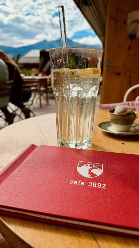 Eine rote Speisekarte mit dem Café 3692 Logo und ein erfrischendes Getränk mit Zitrone auf der Terrasse in Grindelwald.