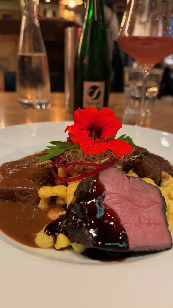Ein fein angerichtetes Wildgericht mit Spätzle, Beeren und einer Kapuzinerkresse-Blüte im Café 3692 Grindelwald.