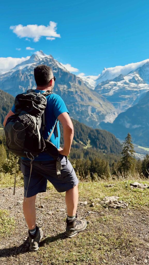 Matthias von Hike&Dine steht mit Rucksack auf dem Wanderweg und blickt auf das Bergpanorama von Grindelwald.