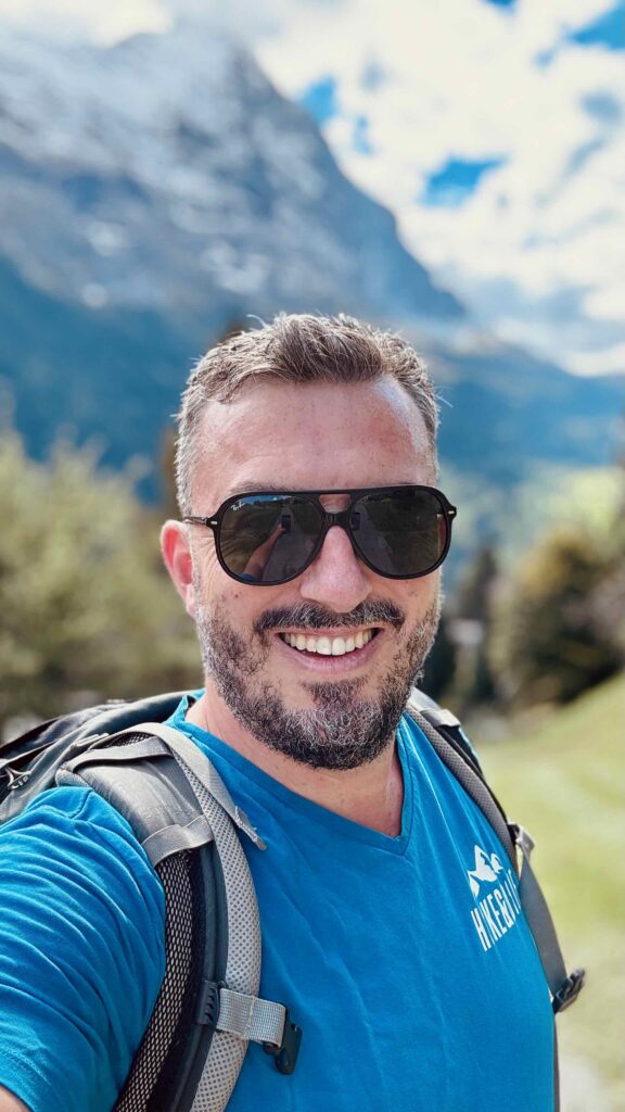 Matthias von Hike & Dine lächelt in die Kamera (Selfie) vor der beeindruckenden Eiger-Nordwand in Grindelwald.
